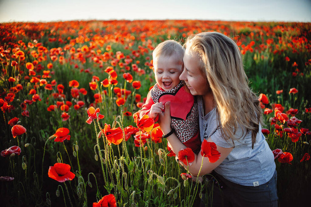 Küçük bir kız ve annesi çiçeklerle ve gelincik tarlasında güneşle mutlu. - Fotoğraf, Görsel