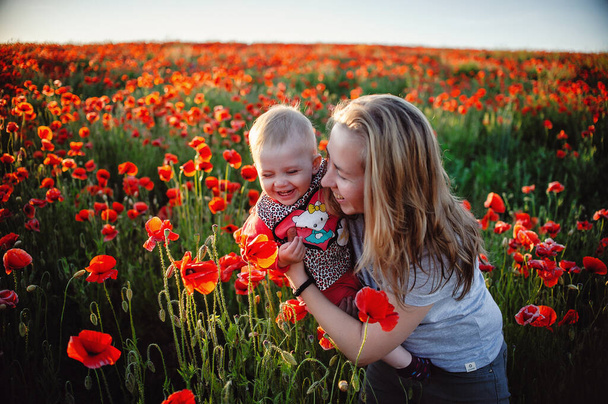 小さな女の子と彼女の母親はケシ畑で花と太陽に満足しています - 写真・画像