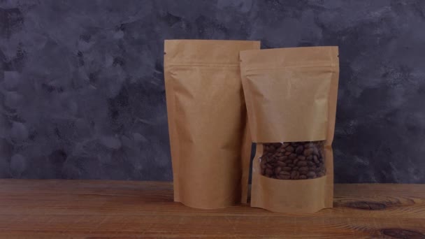 Χέρι σε προστατευτικά γάντια κρατά καφέ Kraft χάρτινη σακούλα σακουλάκι με κόκκους καφέ ξύλινο φόντο 4K mockup. Συσκευασία για το πρότυπο αγαθών παράδοσης τροφίμων. Συσκευασία με κούμπωμα παράθυρο τσάι φύλλα βάρος προϊόντος. - Πλάνα, βίντεο