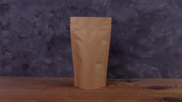 Ruční ochranné rukavice drží hnědé kraft papírové sáček s kávovými zrny dřevěné pozadí 4K mockup. Balení pro dodávání potravin šablony zboží. Balení s uzávěrem okno čaj listy váha produktu. - Záběry, video