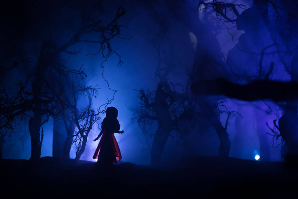 Samotna dziewczyna w martwym lesie w mglistą noc. Sylwetka dziewczyny stojącej między drzewami w świetle księżyca. Pomysł na Halloween. Skupienie selektywne. - Zdjęcie, obraz