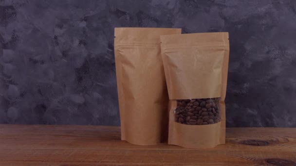 Hand in protective gloves holds brown kraft paper pouch bag with coffee beans wooden background 4K mockup. Packaging for food delivery goods template. Pack with clasp window tea leaves weight product. - Footage, Video