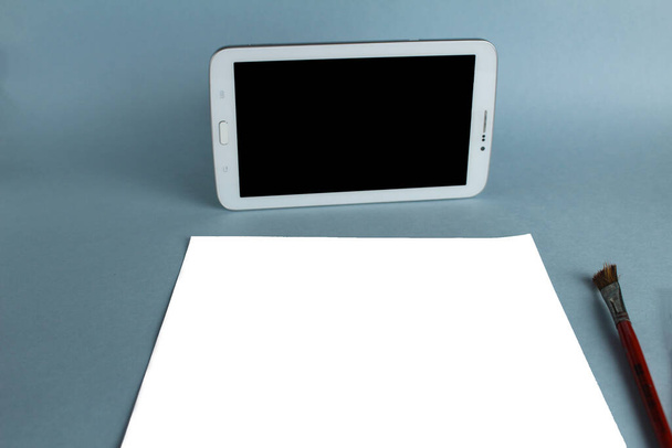 Tabletka do rysowania online i arkusz białego papieru na jasnoniebieskim tle z makietą i miejscem na tekst. - Zdjęcie, obraz