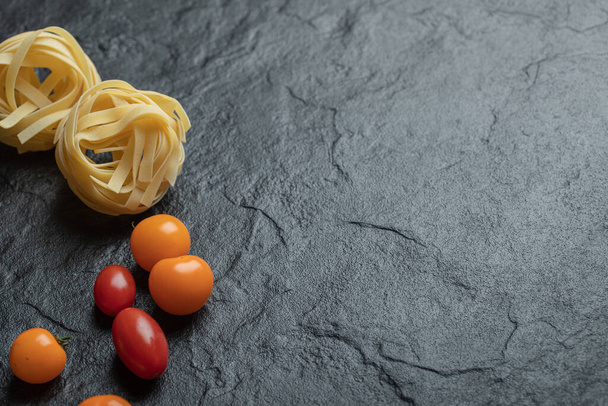 Uncooked nest pasta with cherry tomatoes on a dark background - Photo, Image