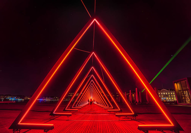 Series of triangular gates of light or intense red light tunnel. The gate of light installation consists of a succession of gates (triangles) where blurred people look like across an extraterrestrial world or coming from the unknown - Photo, Image
