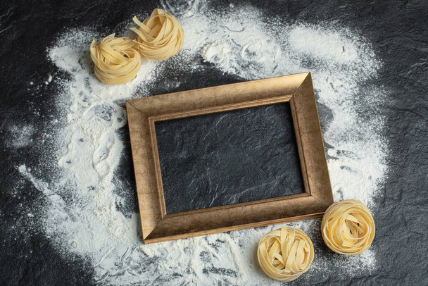 Raw nest pasta with flour and frame on a dark background - Photo, Image