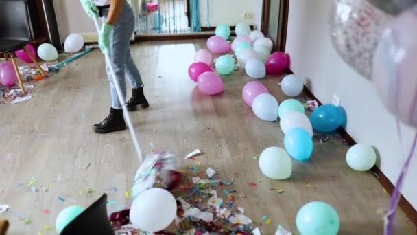 Slow motion, Woman with pushbroom cleaning mess of floor in room after party confetti, morning after party celebration, housework, cleaning service - Footage, Video