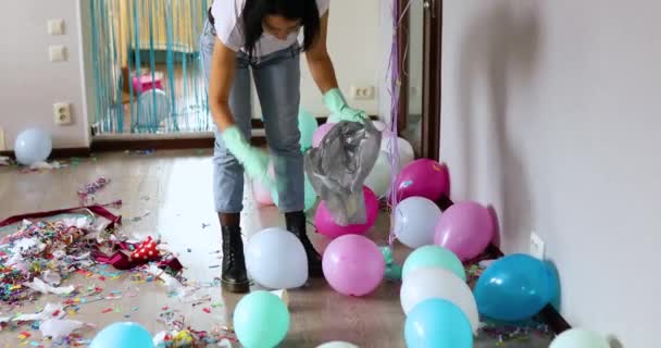 Woman cleaning mess of floor in room after party, removes garbage from the floor, disposable cups in a bag, morning after party celebration, housework, cleaning service - Footage, Video