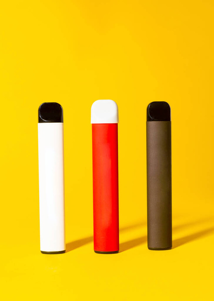 Barevné jednorázové elektronické cigarety se stíny na žlutém pozadí. Koncept moderního kouření, vapingu a nikotinu - Fotografie, Obrázek