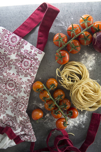 raw tagliatelle pasta, cherry tomatoes, red onion, red and white apron. Healthy eating concept.  - Photo, Image