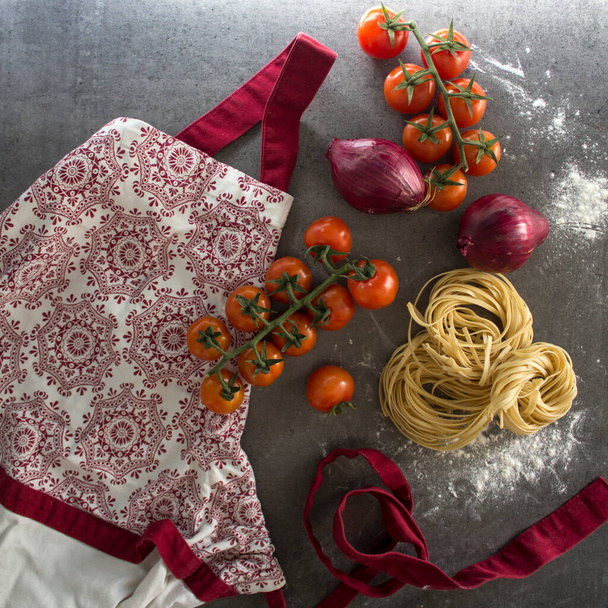 rauwe tagliatelle pasta, kerstomaten, rode ui, rood en wit schort. Gezond eten concept.  - Foto, afbeelding