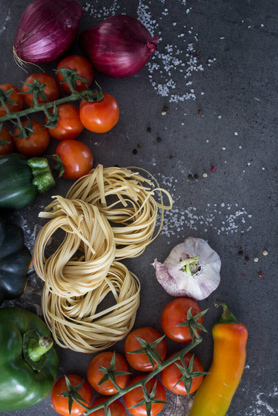 Ingredientes de massa em uma mesa. Esparguete cru e macarrão tagliatelle, tomate cereja e sal marinho sobre fundo cinza texturizado com espaço de cópia. Conceito de alimentação saudável. - Foto, Imagem