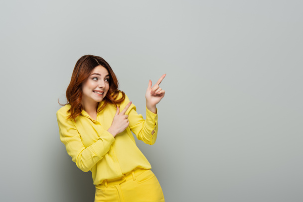 cheerful woman pointing with fingers while looking away on grey - Photo, Image