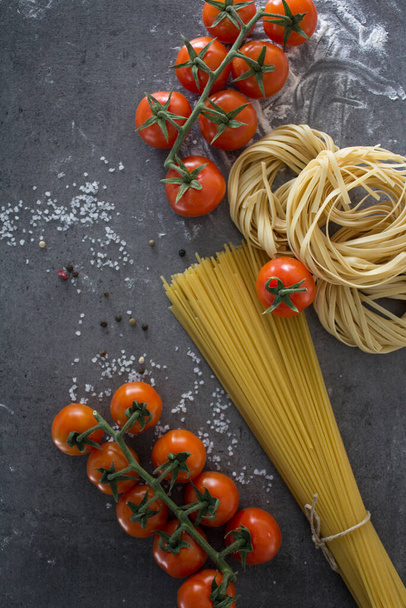 Raw pasta close up photo. Tagliatellepasta and cherry tomatoes on a table. Healthy eating concept. - Photo, Image