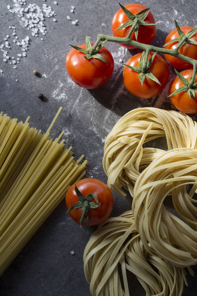 Pasta Tagliatelle, espaguetis y tomates cherry sobre fondo gris texturizado. Comida italiana. Ingredientes frescos vista superior foto. - Foto, Imagen
