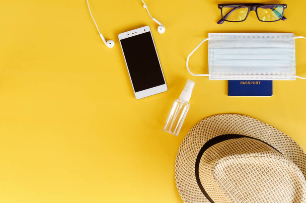 Travel after Covid-19 and new normal concepts. Top view of medical face mask, hand gel sanitizer, headphones and beach hat on yellow background close up. Creative ideas of prevent coronavirus. - Photo, Image