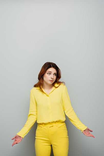 confusa donna in camicetta gialla distogliendo lo sguardo e mostrando gesto scrollata di spalle sul grigio - Foto, immagini