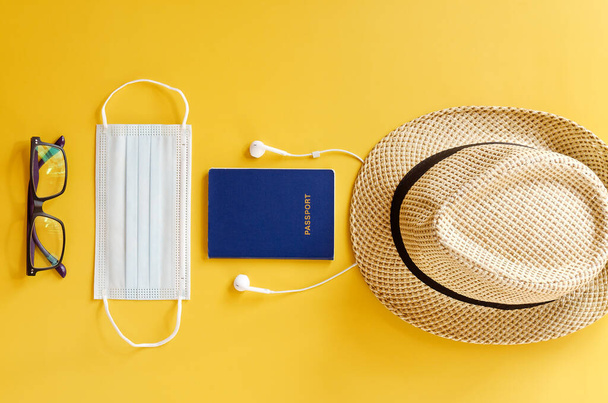 Travel after Covid-19 and new normal concepts. Top view of medical face mask, passport, hand gel sanitizer, headphones and beach hat on yellow background. Creative ideas of prevent coronavirus - Photo, Image