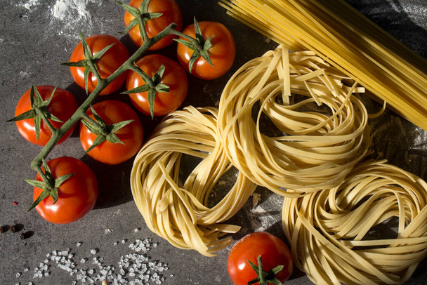 Massa Tagliatelle, esparguete e tomate cereja sobre fundo cinzento texturizado. Comida italiana. Ingredientes frescos vista superior foto. - Foto, Imagem