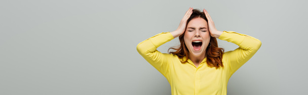 mulher zangada gritando enquanto estava de pé com os olhos fechados e tocando a cabeça no cinza, banner - Foto, Imagem