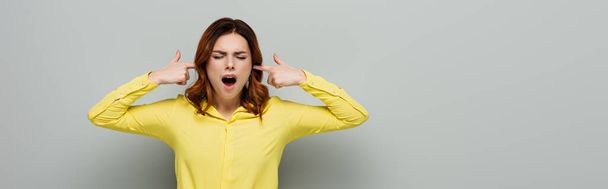 mujer irritada gritando mientras tapaba las orejas en gris, pancarta - Foto, Imagen