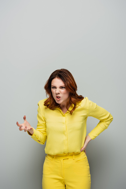 donna irritata con smorfia arrabbiata mostrando gesto spaventoso mentre in piedi con mano sull'anca sul grigio - Foto, immagini