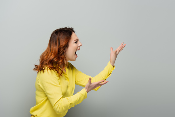 geïrriteerde vrouw in geel shirt schreeuwen terwijl wijzend met handen op grijs - Foto, afbeelding