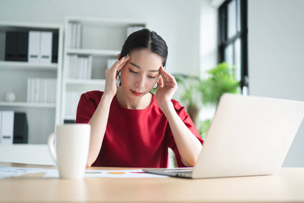 Portret Azjatki pięknej biurowej kobiety z bólami głowy, stresującej pracą, przygnębionej lub mającej gorączkę podczas pracy w biurze, koncepcja presji ze strony pracy, styl życia, stresująca praca. - Zdjęcie, obraz