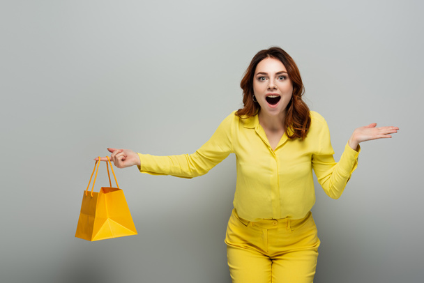 izgatott nő gazdaság sárga bevásárló táska és mutató kézzel szürke - Fotó, kép