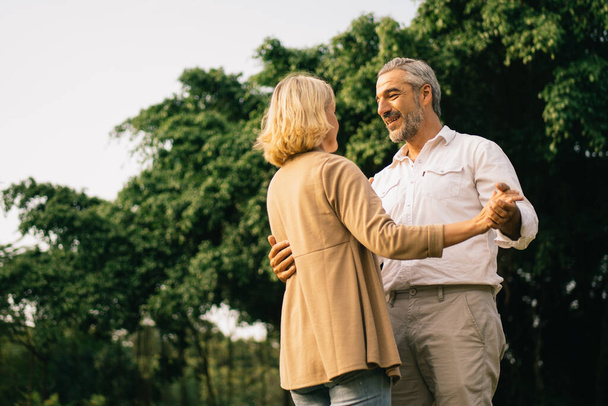 Senior elegant caucasian couple dancing looking at each other feeling love and cherish on their anniversary in the park with copy space, happily retired spouse, well-managed retirement life concept. - Photo, Image