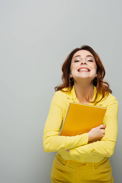 fröhliche Frau mit Notizbuch lächelt in Kamera auf grau - Foto, Bild