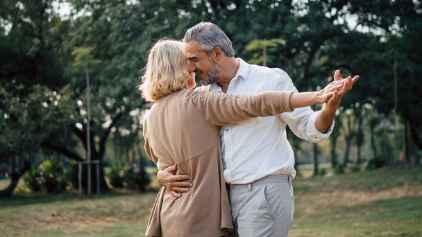 Idősebb, elegáns, kaukázusi pár táncol, nézik egymást, szeretik és ápolják egymást az évfordulójukon a parkban, fénymásoló hellyel, boldog nyugdíjas házastárssal, jól menedzselt nyugdíjas életfelfogással.. - Fotó, kép
