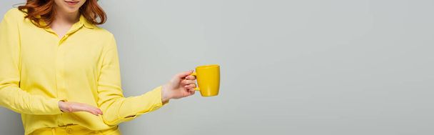 partial view of woman pointing at yellow cup on grey, banner - Photo, Image