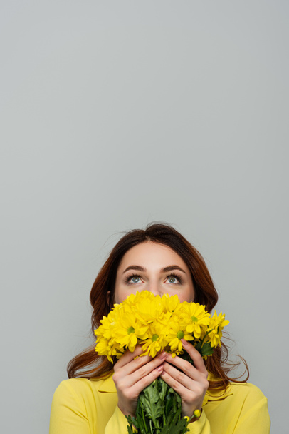 zufriedene Frau blickt auf, während sie ihr Gesicht mit gelben Blüten auf grau verdeckt - Foto, Bild