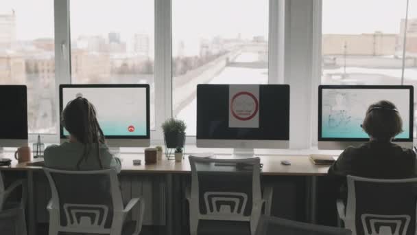 PAN-kuva nuorista mies- ja naispuolisista puhelinkeskuksen agenteista, jotka istuvat tietokoneen monitorien edessä panoraamaikkunoiden ja sosiaalisen etäisyyden kautta puhuessaan asiakkaiden kanssa äänipuheluissa - Materiaali, video