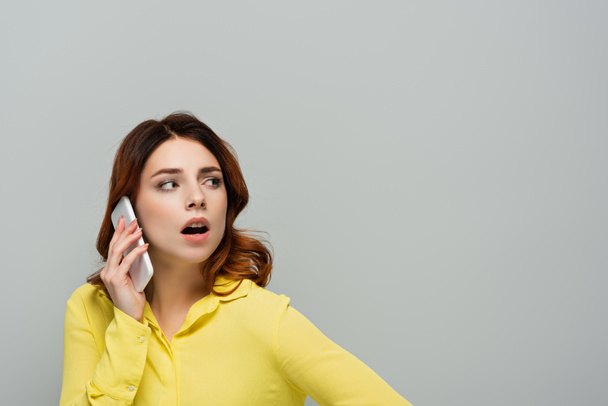 surprised woman talking on smartphone and looking away isolated on grey - Photo, Image