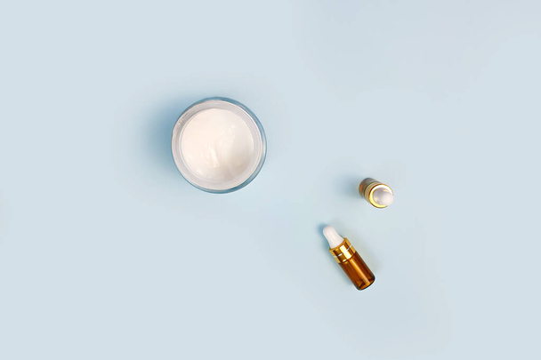Top view of open cream jar and glass bottles with pipette on blue table. Skin care, moisturizing beauty products, lifestyle, skincare consept - Photo, Image