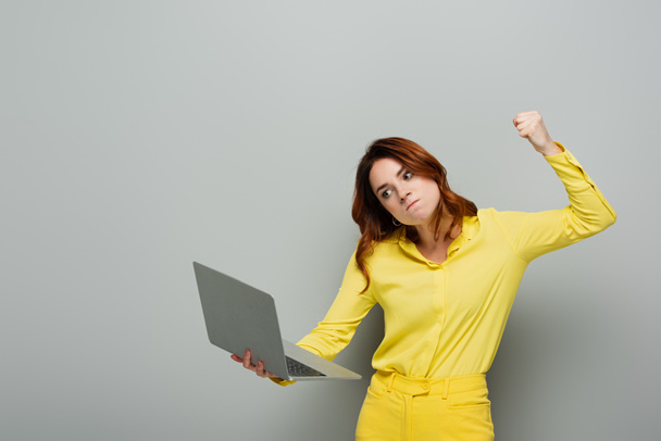 dühös nő kezében laptop miközben áll összeszorított ököllel szürke - Fotó, kép