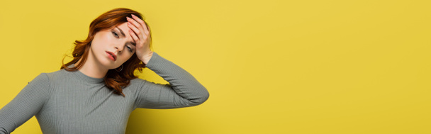 mujer cansada mirando a la cámara mientras sufre de dolor de cabeza en amarillo, pancarta - Foto, Imagen