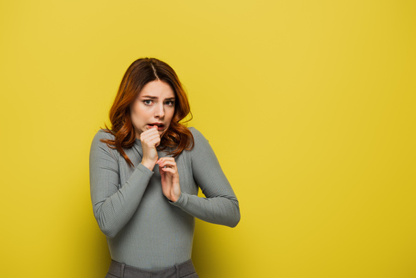 anxious woman looking at camera while holdings hands near face on yellow - Photo, Image