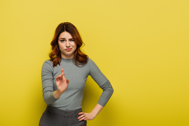 δυσαρεστημένη γυναίκα στέκεται με το χέρι στο ισχίο και δείχνοντας με το δάχτυλο, ενώ δεν δείχνει κανένα σημάδι στο κίτρινο - Φωτογραφία, εικόνα