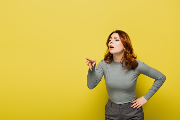 donna con i capelli ricci in piedi con mano sul fianco mentre punta con il dito sul giallo - Foto, immagini
