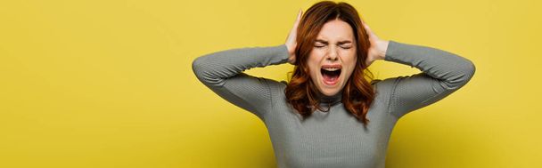 young woman screaming while touching head on yellow, banner - Foto, Imagen