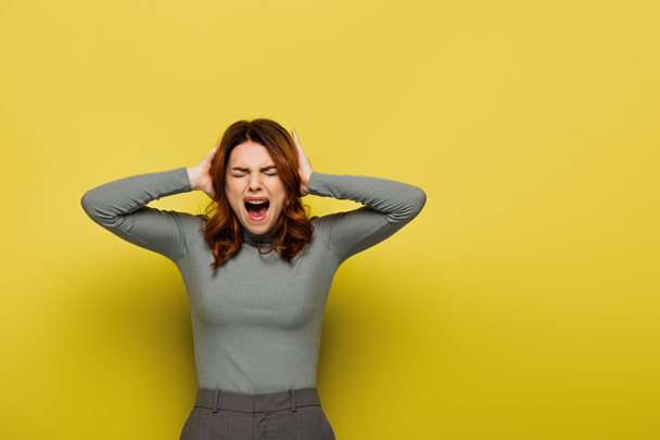 young woman screaming while touching head on yellow - Фото, зображення