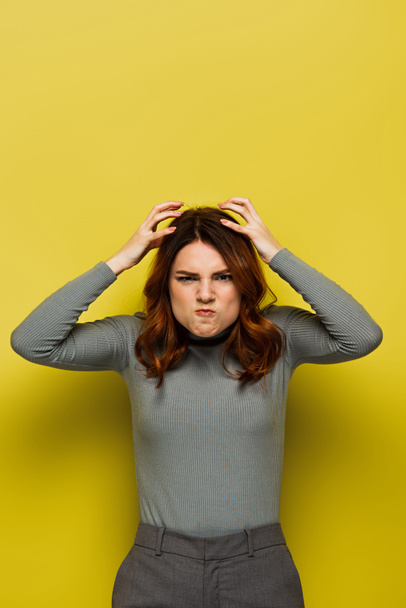 stresovaná žena s kudrnatými vlasy dotýkající se hlavy a při pohledu na kameru na žluté - Fotografie, Obrázek