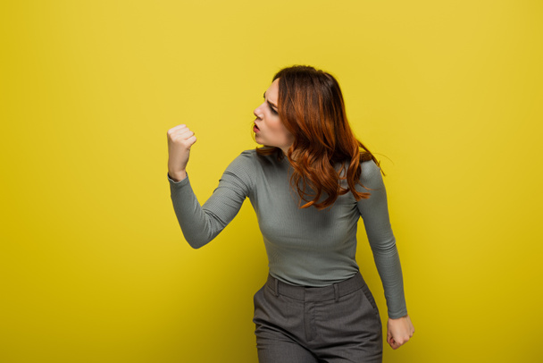 mulher zangada com cabelo encaracolado mostrando punho apertado no amarelo - Foto, Imagem