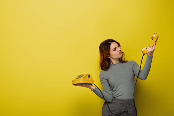mujer joven disgustado mirando teléfono retro en amarillo - Foto, Imagen
