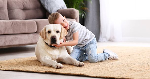 Полное тело улыбающегося маленького мальчика, обнимающего очаровательную чистокровную собаку-лабрадора, пока мы проводим время вместе дома - Фото, изображение