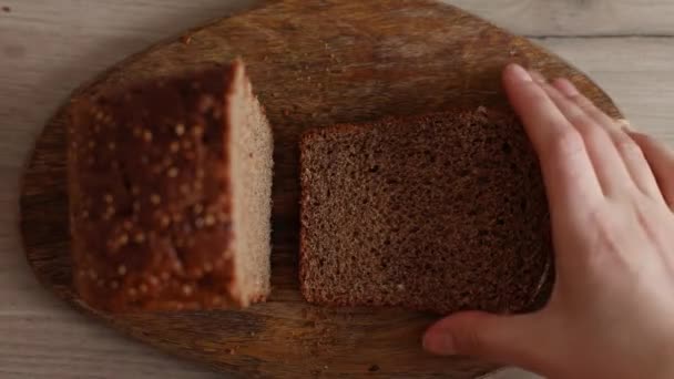 Nahaufnahme eines Mannes, der ein Stück Brot nimmt. Hand nimmt frisches Scheibchen Brot auf Holzbrett - Filmmaterial, Video