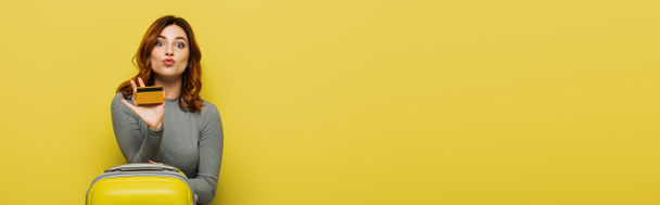 femme aux cheveux bouclés tenant bagages et carte de crédit isolée sur jaune, bannière - Photo, image